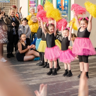 Young children dancing in bright colours as part of a street performance.