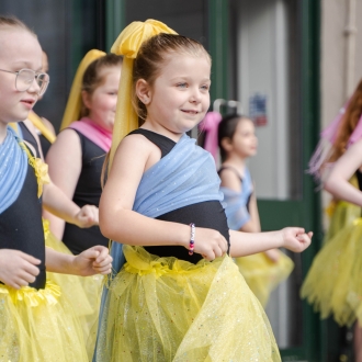Young children dancing in bright colours as part of a street performance.