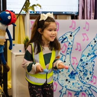 A pre-school aged child wearing a hi-vis next to an artwork of a Liver Bird.