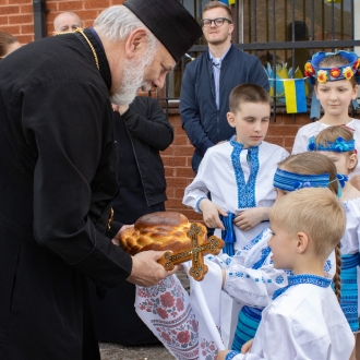 A man accepting bread outside of the Ukrainian Community Centre from children dressed in traditional Ukrainian dress.