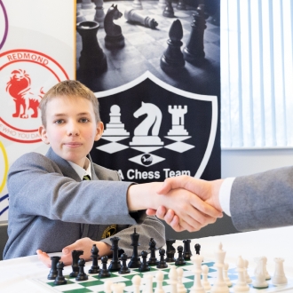 A secondary school pupils shaking his opponents hand before staring a game of chess.