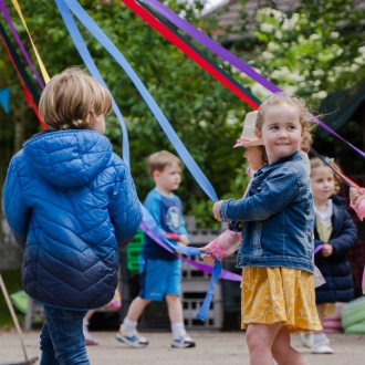 Pre-schoolers dancing around a circle holding ribbons.