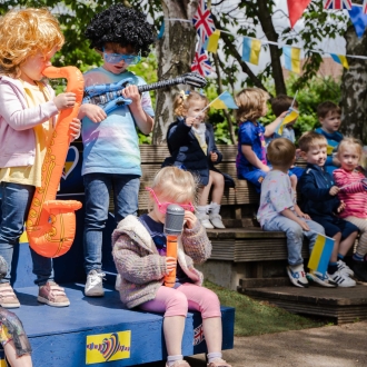 Pre-school aged children doing a Eurovision-themed performance outside.