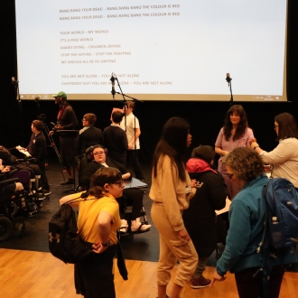 A choir group practicing a performance with lyrics on the screen.