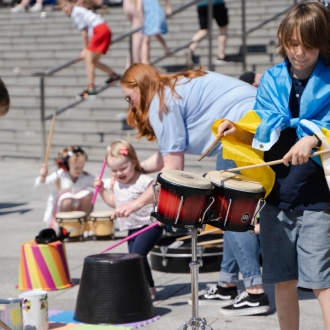 A young boy playing drums at an interactive busking performance.