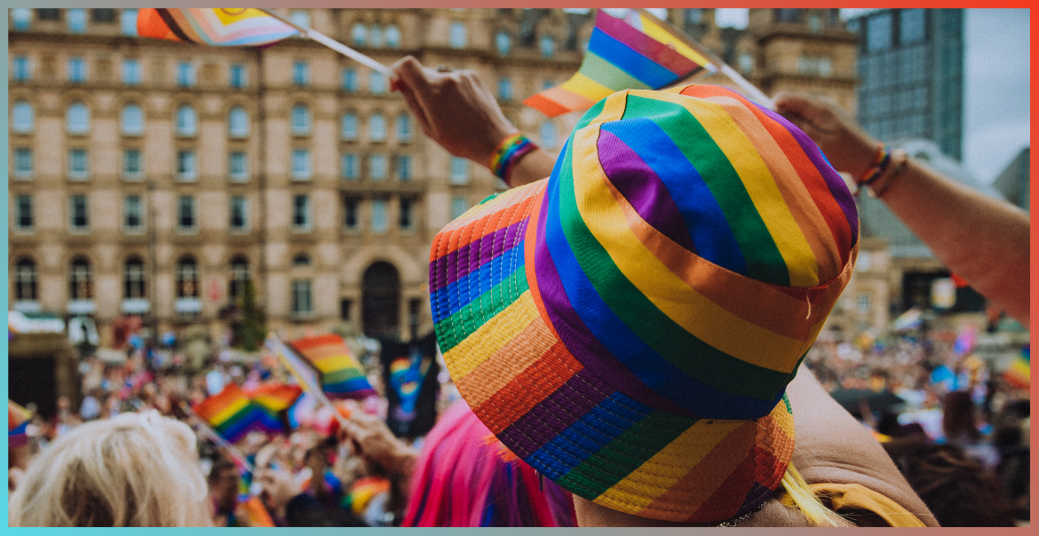 A person wearing a rainbow coloured bucket hat waving a handheld pride flag.