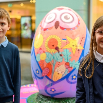 Two children next to a large egg sculpture part of the Pysanka Egg display in Liverpool One high street.