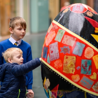 Two children touching a large egg sculpture part of the Pysanka Egg display in Liverpool One high street.