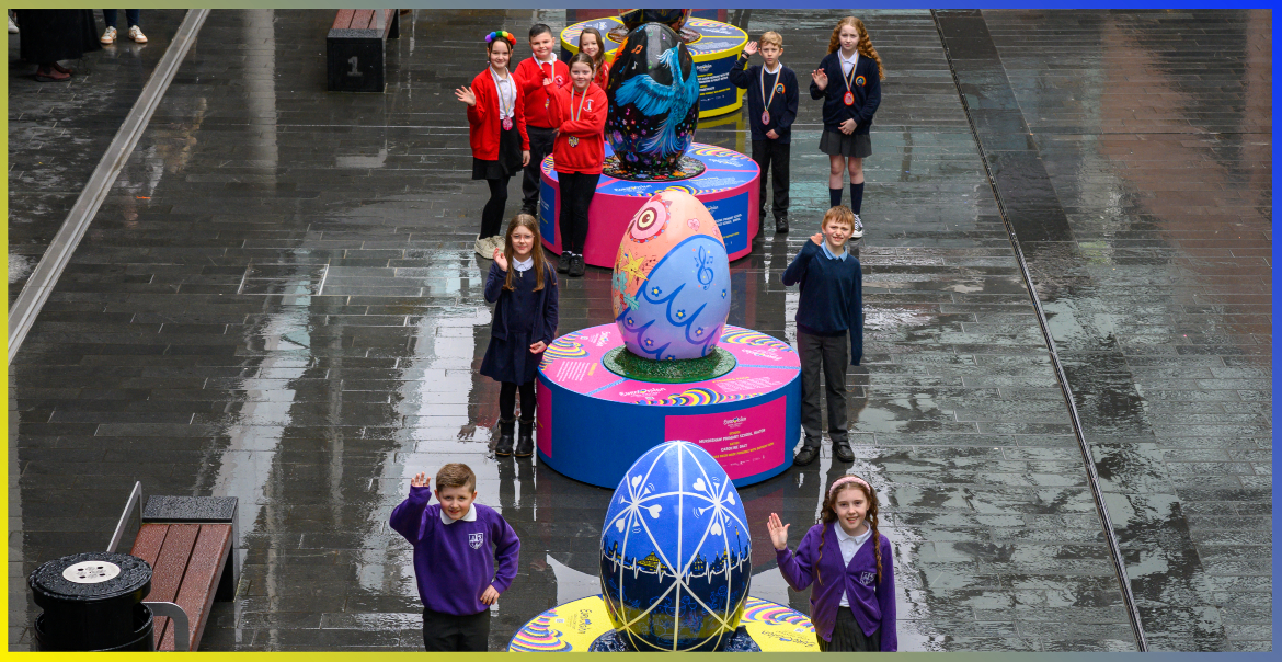 Three large scale egg sculptures with primary school children stood next to each one.