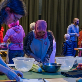 Adults and children working together around a communal table to prepare a meal.