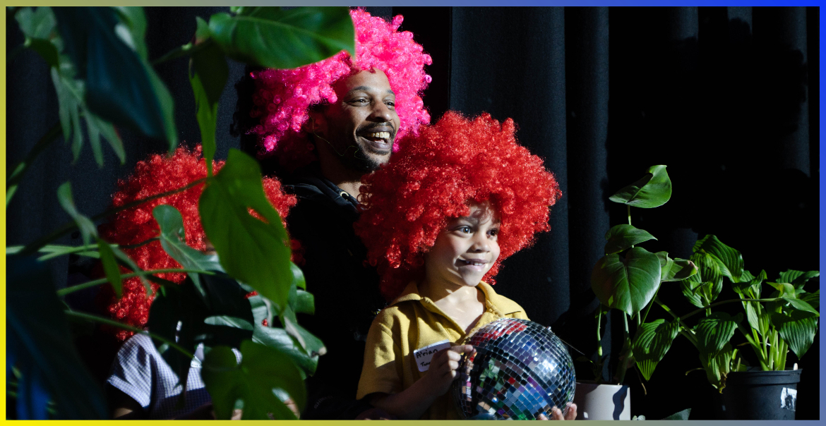 A man and child wearing colourful wigs and holding a mirror ball.