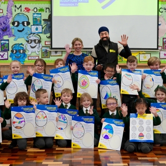 A primary school class holding up their designs for Pysanka Eggs along with a teacher and artist.