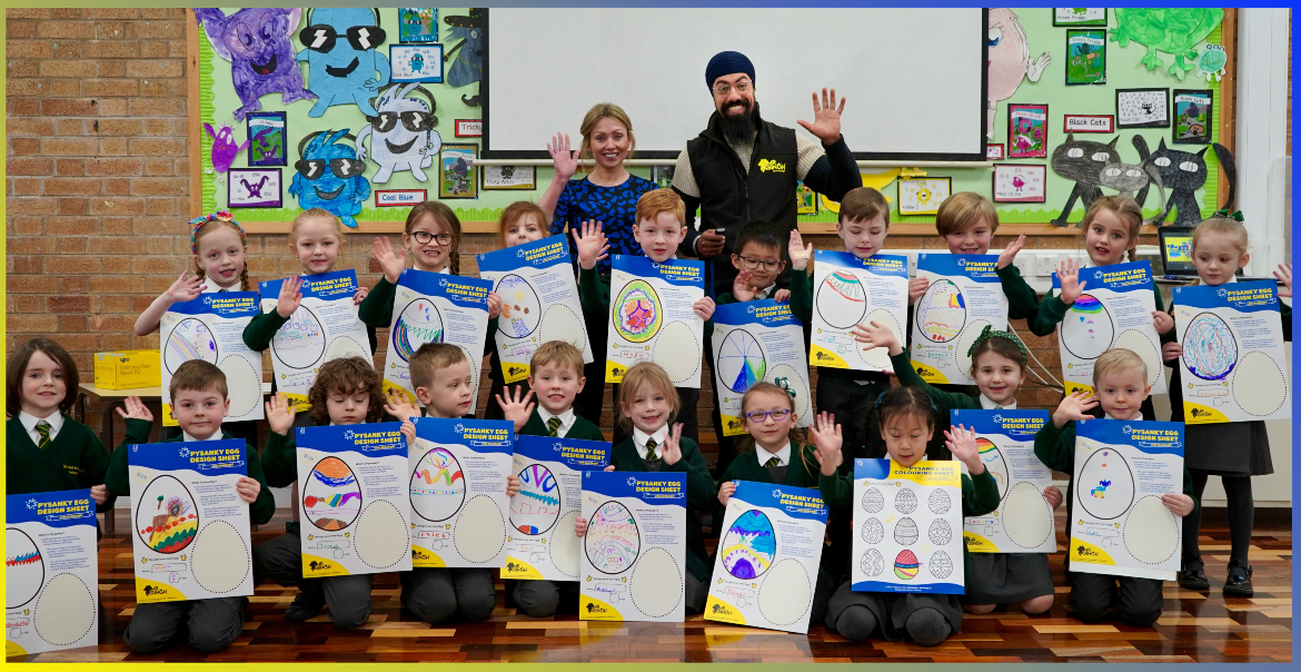 A class of primary school pupils along with their teacher and an artist holding up their own designs of Pysanka Eggs.