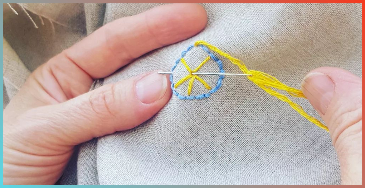 A hand stitching a pattern into a tablecloth.