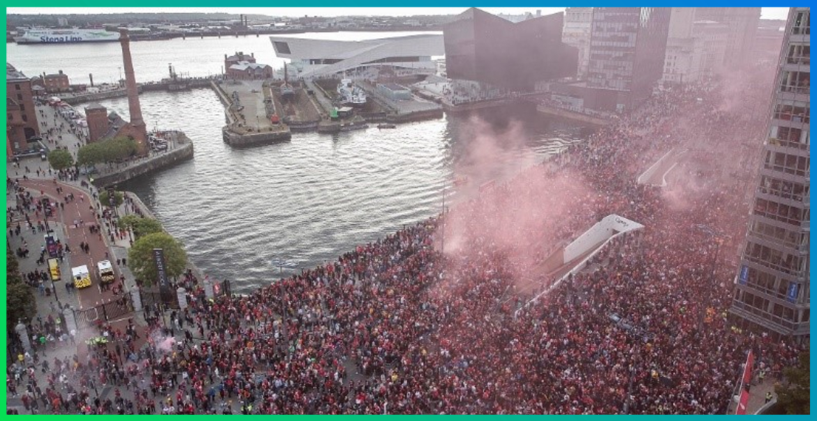 Liverpool's waterfront filled with crowds as the Liverpool Football Club celebration parade passes through with red smoke.
