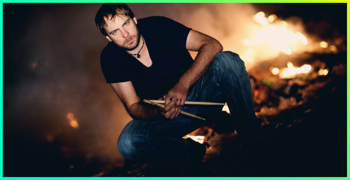 A man crouching down holding drumsticks.