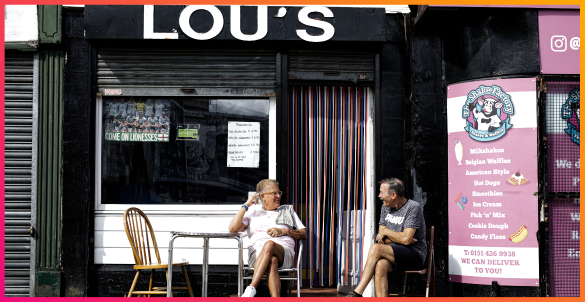 A photograph of the exterior of LOU'S cafe with two people sitting outside at a table.