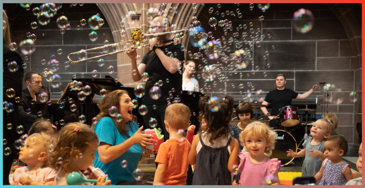 Children dancing on a dance floor while a band plays with bubbles floating all around.