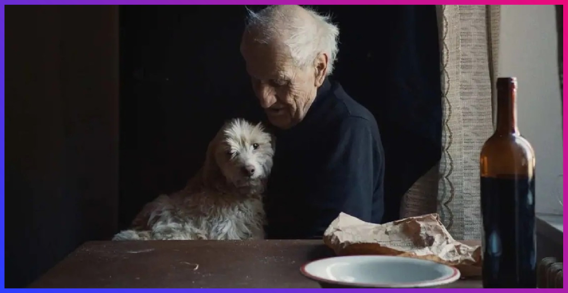 An older man with a white dog on his knee at the dinner table.