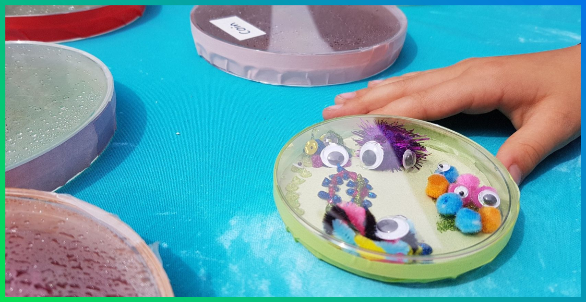 child's hand holding a petri dish full of googly eyes and other crafting bits