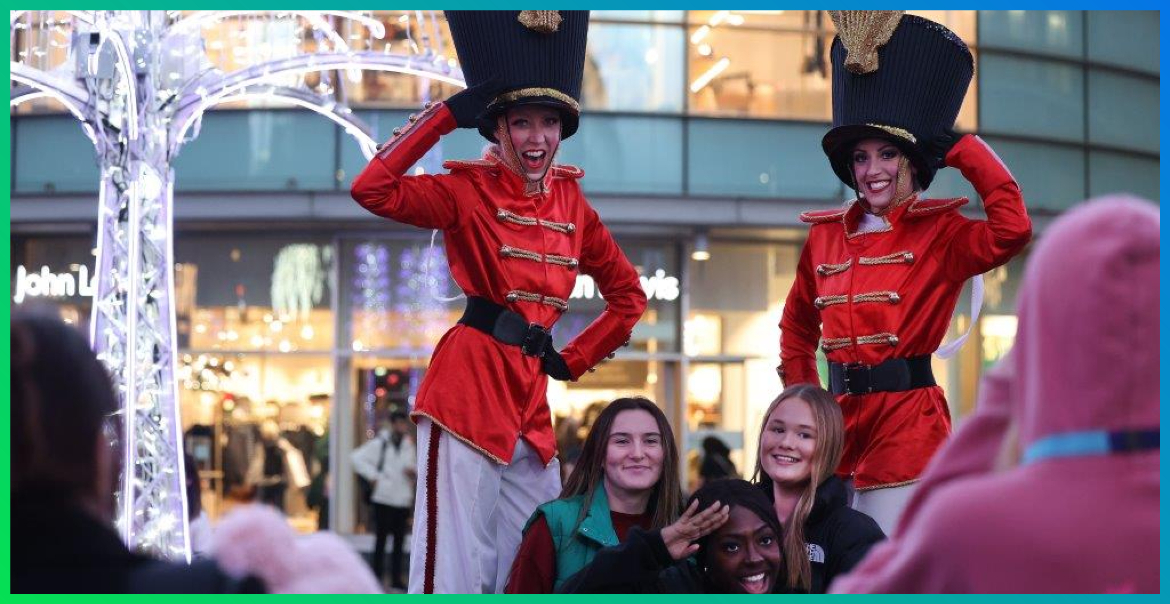 Two stilt performers dressed as Christmas soldiers, posing for a photo with a group of friends in Liverpool ONE.