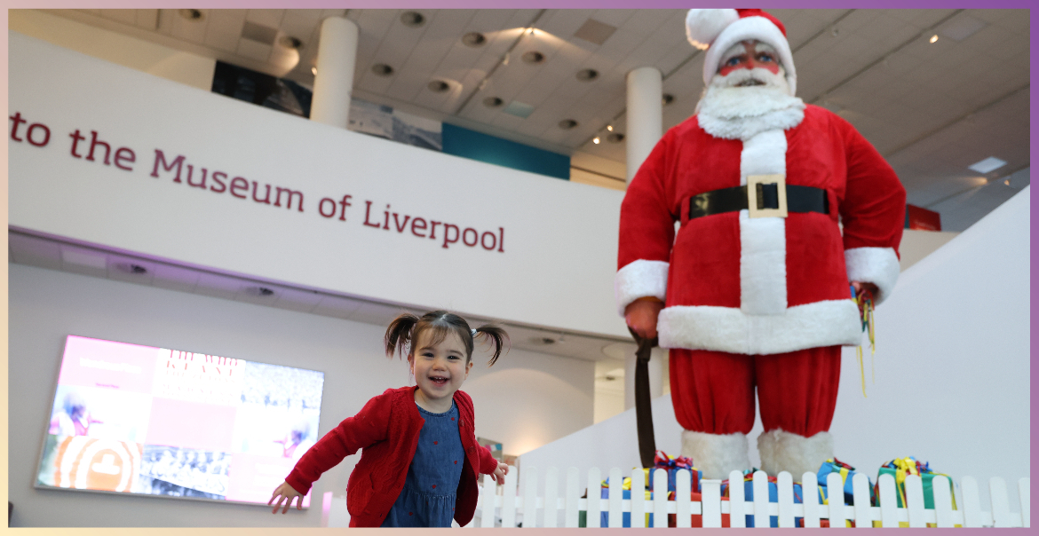 A giant santa figure in Museum of Liverpool. A toddle is playing in front of it.