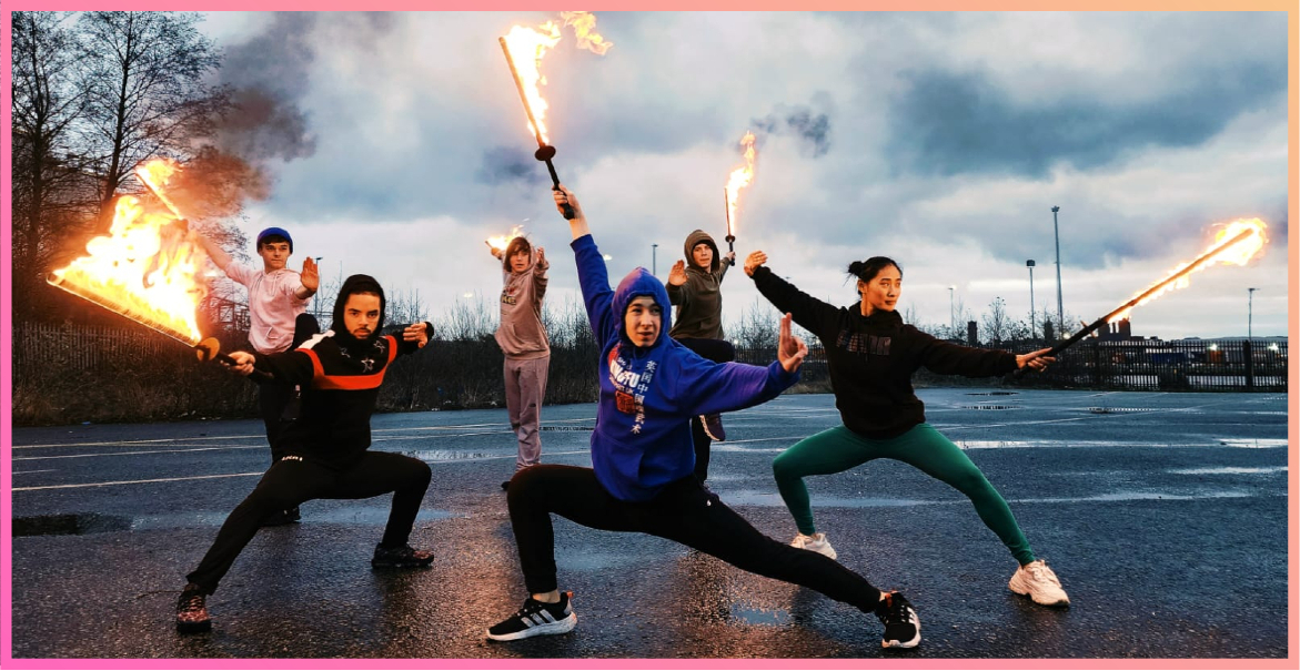 group of young artists standing on tarmac in various poses holding swords that are on fire