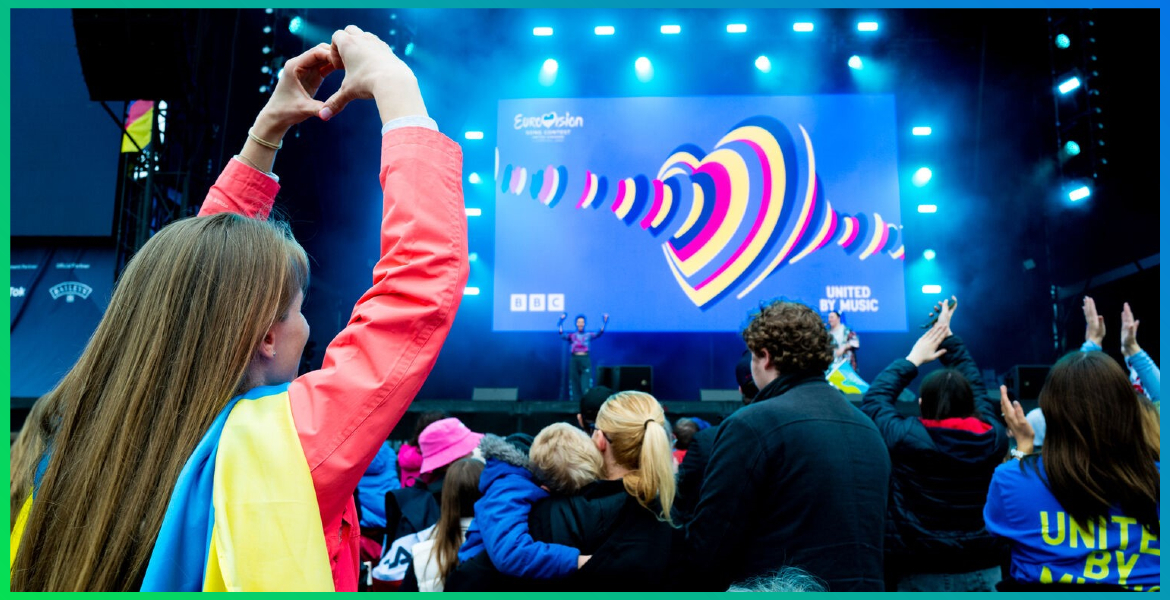 a crowd in front of a stage in Liverpool as part of EuroFestival 2023, with a girl holding her arms up in the air making a heart shape with her hands