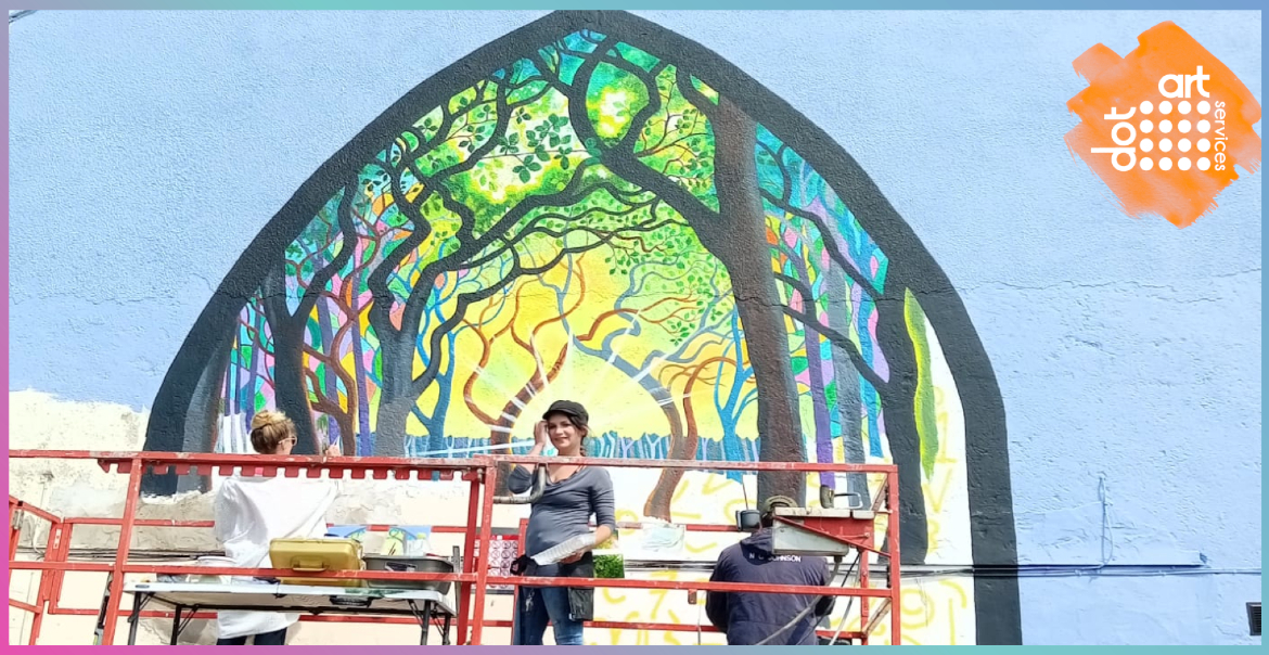An artist painting a mural on a large exterior wall.