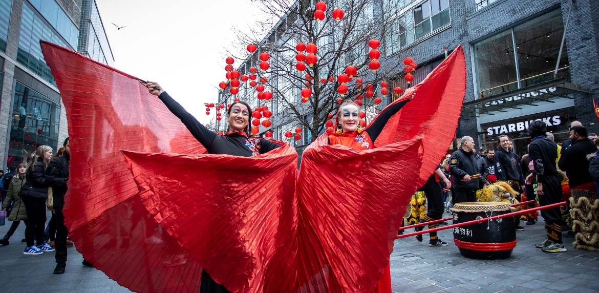 two dancers in red costumes pose in front of a tree adorned with red Chinese lanterns in Liverpool ONE