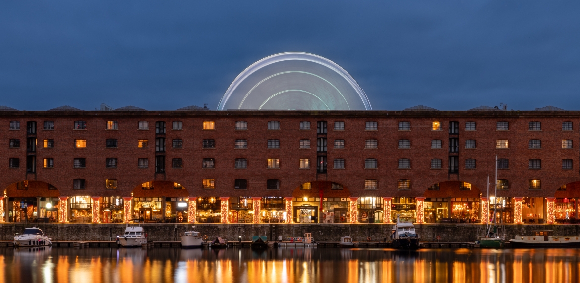Royal Albert Dock Liverpool at dusk with lights reflecting in the water and the big wheel illuminated in the background