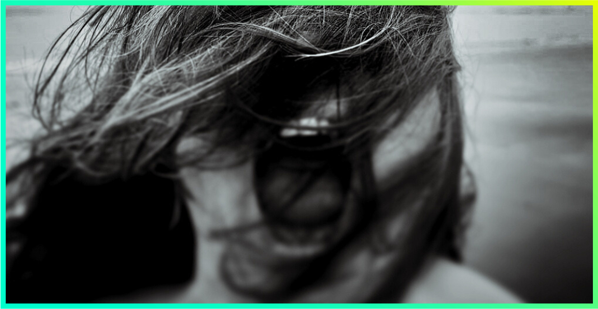 black and white image of a lady at the beach with her hair blowing across her face screaming