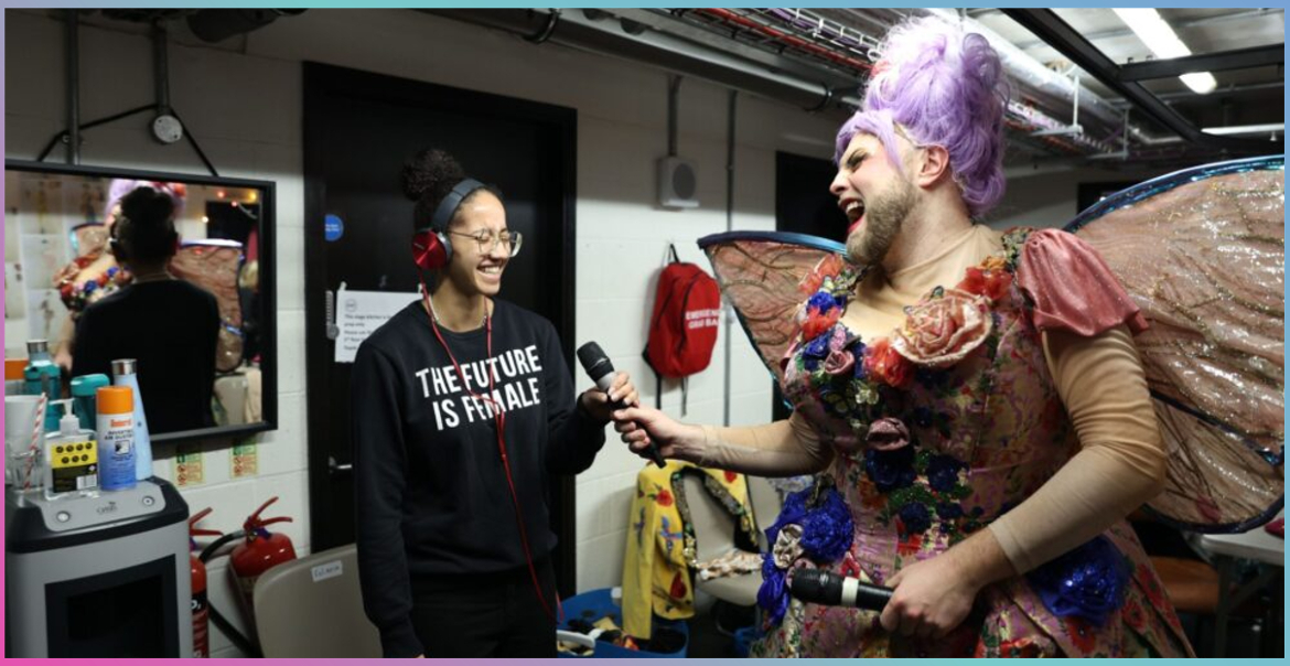 A performer dressed for a pantomime backstage with one of the crew.