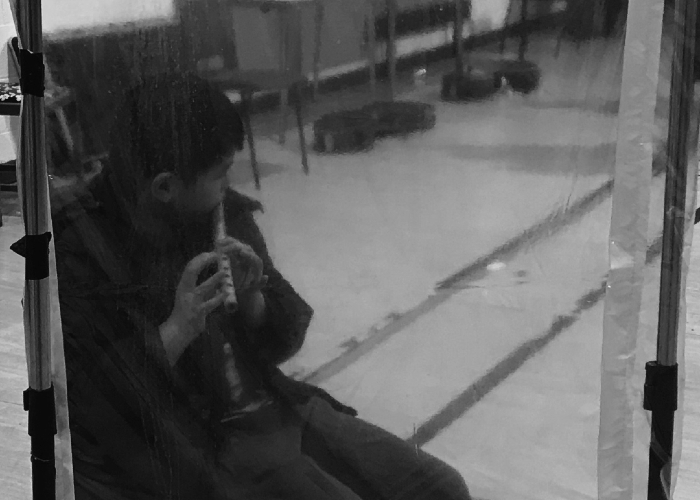 Picture of a boy practising the flute behind a screen during lockdown