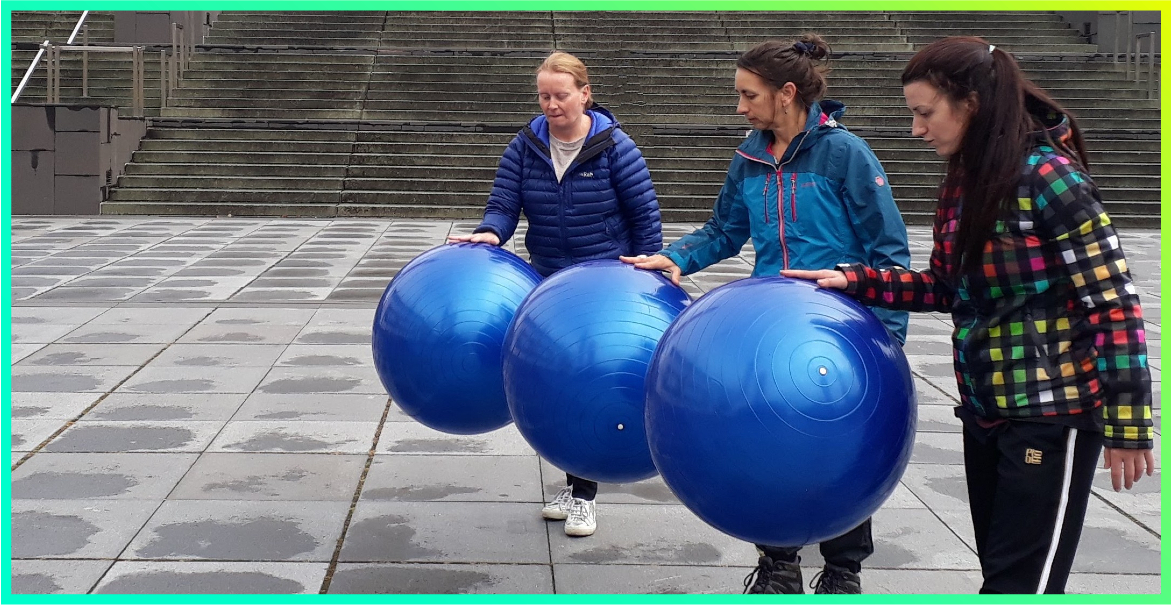 a picture of three women standing on a pavement in front of steps bouncing three large inflatable balls