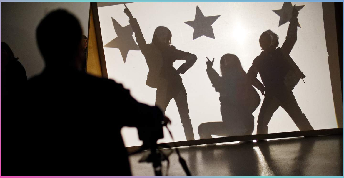 Silhouettes of children posing in a formation with star shapes behind a sheet.