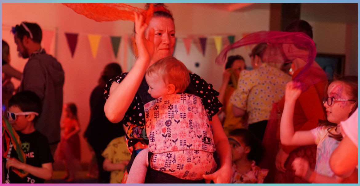 A woman carrying a small child while dancing at a family friendly disco.