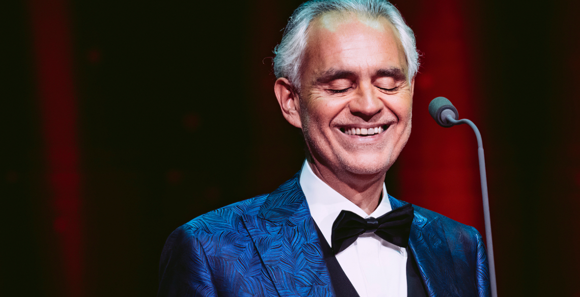 picture of Andrea Bocelli dressed in a blue jacket, white shirt and black dickie bow smiling with his eyes closed