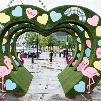 Three green hearts structures in an outdoor setting with pastel coloured mini hearts and flamingos decorating onto the structure.