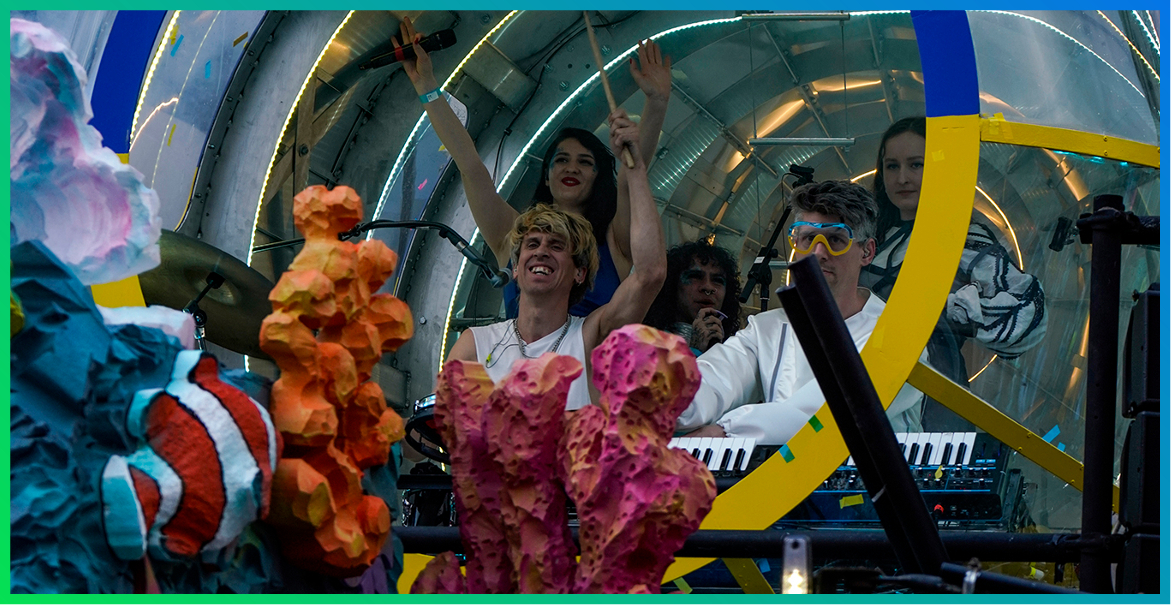 group of people sitting inside a blue and yellow submarine surrounded by coral and fish puppets