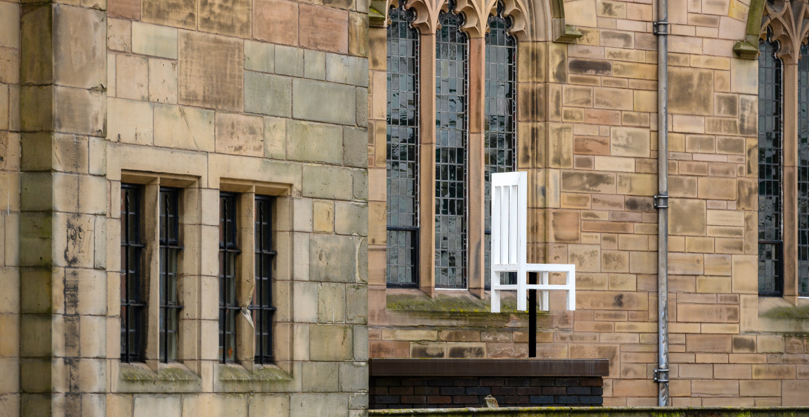 A white chair sculpture suspended near a church wall.