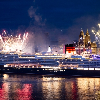 Queen Anne ship leaving Livepool at night with the iconic waterfront and fireworks in the background.