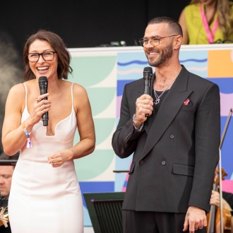 A female and male presenter on stage at an outdoor event.