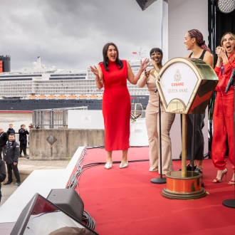On stage for the naming ceremony of Queen Anne, five women pull the lever to name the ship.