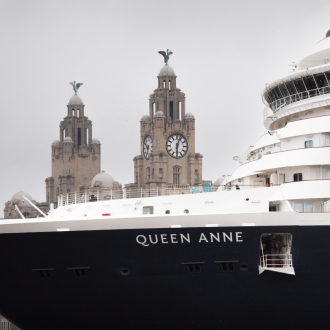 A close up image of Cunard Queen Anne ship docked in Liverpool on an overcast day with the Royal Liver Building in the background.