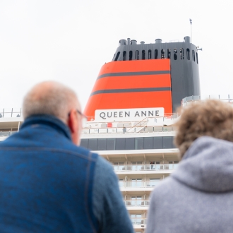 A close up image of Cunard Queen Anne with two people looking out towards the ship/