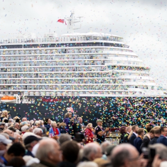 A large crowd over looking the Queen Anne cruise ship on an overcast day as colourful confetti falls in the air.
