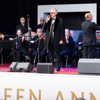 Andrea Bocelli performing on stage with an orchestra at an outdoor event.