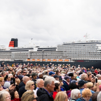 A large crowd over looking the Queen Anne cruise ship on an overcast day.