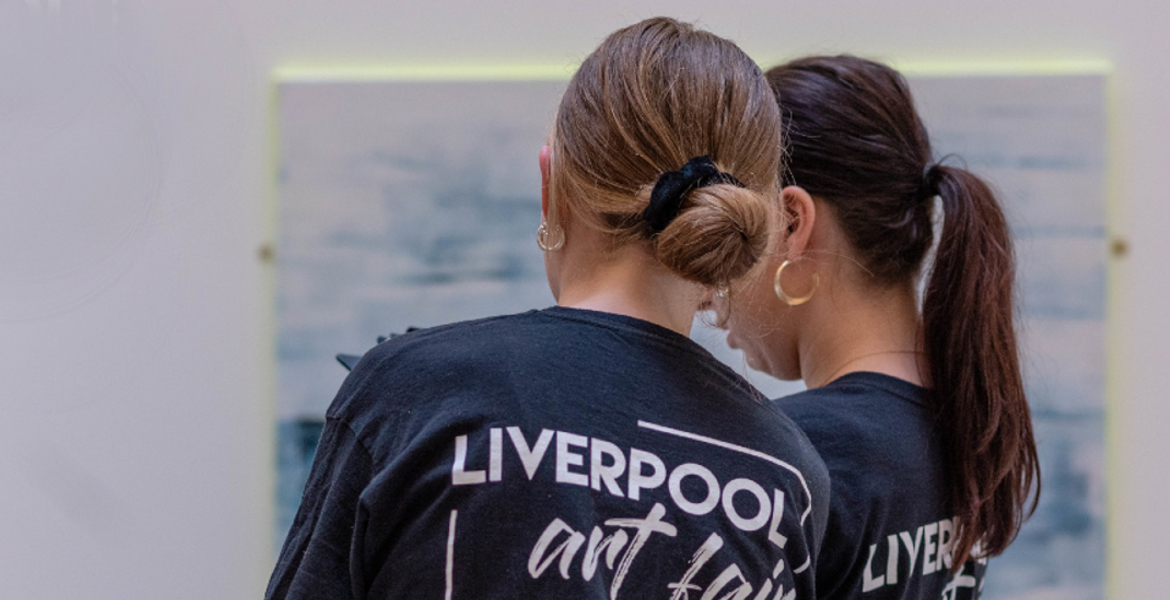Two people wearing black t-shirts with "Liverpool Arts" written on the back, viewing an abstract painting in a gallery.